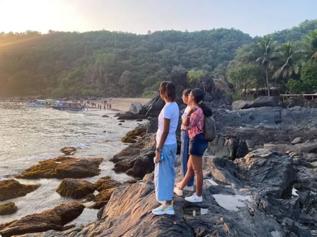 Travelers standing on coastal rocks watching sunset over the bay